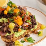 Front view on 2 Mexican black bean toasts on a plate showing nicely the layers of mashed avocado, Mexican style black beans and a quick tomato salsa.