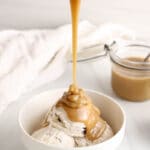 There is a stream of salted tahini sauce pouring over ice cream in a bowl.