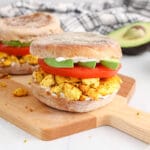 Showing is a vegan tofu scramble breakfast sandwich layered with avocado and tomatoes.