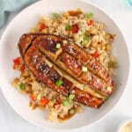 Overhead view on a halved miso glazed aubergine on vegetable rice and topped with sesame seeds and green onion.
