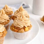 Focus on a vegan carrot cake cupcakes on a plate with more cupcakes in the background.