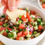 Close up on a tortilla chip dipping in a bowl of cucumber pice de gallo.