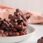 There are a few mini cluster of chocolate covered chickpeas on a plate topped with sea salt.