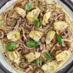 View on a large vegan white sauce funghi pizza topped with artichokes over a baking dish.