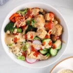 Overhead view on a tofu buddha bowl topped with an Asian peanut sauce and sriracha.