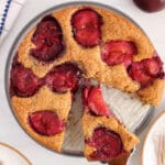 Overhead view on a vegan plum cake with a spatula taken a slice away.