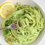 There is a fork taking a portion of noodles in a dairy-free green pasta sauce.
