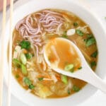 There is a spoon taking some of the broth from a bowl of cabbage miso soup.
