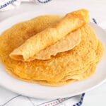 There are a few red lentil tortilla wraps on a plate with some red lentils in the background.