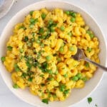 Showing is a bowl of vegan mac and cheese made without cashews and tossed with green peas and topped with parsley.