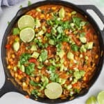 Overhead view on large Cajun orzo skillet with beans and a tomato sauce. Topped with cilantro and lime wedges.