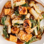 Close up on a easy bok choy tofu stir fry garnished with sesame seeds with the focus on a cube of roasted tofu.