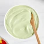 Close up on a small bowl of vegan avocado crema with a wooden spoon to show the whipped consistency.