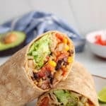 Close up on a vegan black bean burrito stuffed with rice and avocado that's sliced in half to show the middle.
