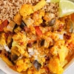Close up on a bowl filled with a brown rice and a saucy aubergine and cauliflower curry stew.
