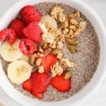 Close up on a creamy bowl of warm chia seed pudding topped with banana, berries and granola.