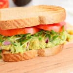 Close up on a vegan chickpea avocado sandwich made with sprouts and slices of tomatoes.