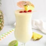 Front angle view showing a tall glass of a piña colada mocktail decorated with maraschino cherries and pineapple wedges.