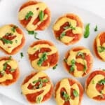 Overhead view on a platter with a few vegan bagel bites topped with fresh basil.