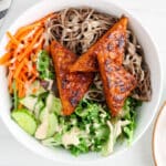 Showing is a vegan marinated tempeh that was fried in a pan and laying over noodles and lettuce.