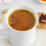 Angle view on a cup of turmeric hot chocolate with peanut butter cookies in the background.
