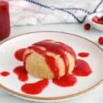 There is a small white cake on a plate with a drizzle of cranberry coulis over.