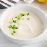 Front angle view on a bowl of vegan tofu sour cream topped with green onion and with some lemon in the background.