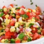 Showing a pico de gallo made with tomatoes, jalapeño and red onions in a bowl with a spoon.