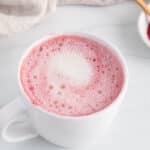 Front angle view on a white mug of pink latte made with red beet powder.