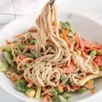 There are chop sticks taking some veggies-loaded vegan peanut noodles from a bowl.