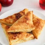There are 4 vegan apple turnovers on a plate with apples on the side.