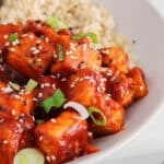 Close up on a cubed gochujang tofu from a bowl topped with sesame seeds and green onions.