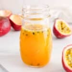 Close up on a passion fruit syrup with some of the seeds floating around and fresh passion fruits on the side.