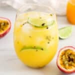 View on a glass of passion fruit mocktail with fresh passion fruits on the side.