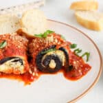 Dairy-free eggplant rollatini on a plate topped with vegan parmesan cheese and fresh basil.