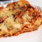 View on a piece of vegan lentil lasagna on a plate showing the layer of noodles, lentil marinara and vegan bechamel.