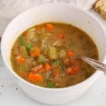 Front angle view on a bowl of carrot celery soup with dill and bread on the side.