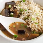 Close up on a Asian style spoon taking some of the miso broth from an eggplant miso soup.