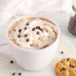 Front angle view on a mug of dairy-free oat milk hot chocolate topped with vegan whipped cream and chocolate chips.