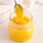 There is a spoon drizzling some mango coulis back in its storing jar.