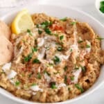 View on a bowl of creamy baba ganoush garnish with vegan yogurt, parsley, spices and a side of pita bread.