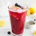 View on a tall glass of blueberry lavender lemonade garnished with lemon slices and fresh blueberries.
