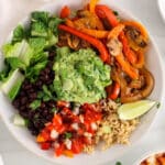 Overhead view on a vegan fajita bowl filled with rice, black beans, fajita vegetables and an avocado mash sauce.