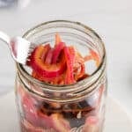 There is a fork taking some pickled red onion from a jar.