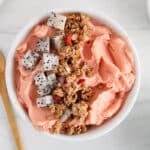 Overhead view on a bowl of watermelon smoothie bowl garnished with granola and cubed dragon fruit.