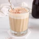 View on a short glass of vegan peanut butter coffee garnished with cacao powder with a small spoon.