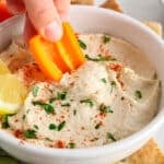 There is a piece of orange pepper dipping in a butter bean hummus.