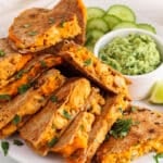 Front angle view on many pieces of vegan buffalo chickpea quesadillas on a plate with a side of avocado mash sauce.