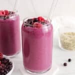 View on 2 glasses filled with a raspberry blueberry smoothie garnished with berries and hemp seeds.