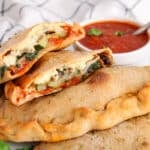View on a plate with a few vegan calzones with one opened up to show filling.